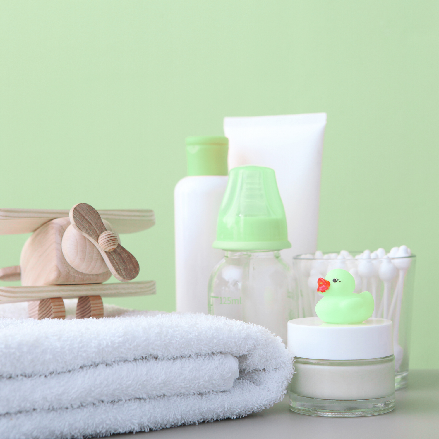 Baby bathroom items including a towel, bottles, and a rubber duck on a light green background